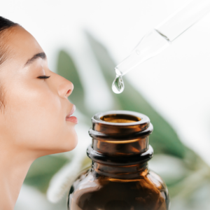 Essential oil drop from a dropper above an open bottle with a side profile of a lady inhaling