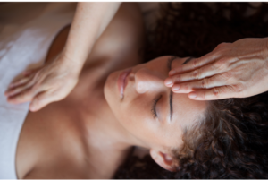 Healing hands on lady lying on a massage table. One hand is on her forehead and the other hand is on her heart