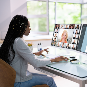 Lady sitting at her desk with headphones on, viewing a screen with pictures of all the participants in a webinar.